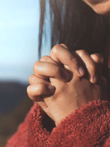 Woman hands folded in prayer in beautiful nature background with sunlight in vintage color tone